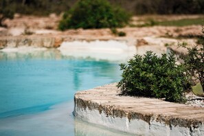 Een zwembad met helderblauw water, omgeven door stenen constructies en groen.