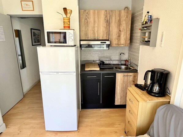 A compact kitchen with a white refrigerator, a microwave, a sink, and a coffee maker.