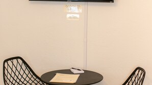 A room with a flat-screen TV mounted on the wall, two black mesh chairs, a small round table with a pen, and a trash bin. - Enjoy the tranquility of a scenic riverside neighborhood in Gold Hill. This area is peaceful, offers beautiful views, and is a convenient stopover location. (Gold Hill)