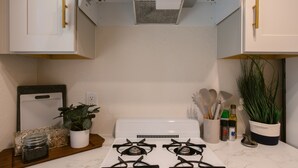 A kitchen with white cabinets, a white stove, a plant, and kitchen utensils. - Enjoy the tranquility of a scenic riverside neighborhood in Gold Hill. This area is peaceful, offers beautiful views, and is a convenient stopover location. (Gold Hill)