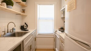 A compact kitchen with a sink, stove, and countertop. There is a window with blinds, and a small plant on a shelf. - Enjoy the tranquility of a scenic riverside neighborhood in Gold Hill. This area is peaceful, offers beautiful views, and is a convenient stopover location. (Gold Hill)