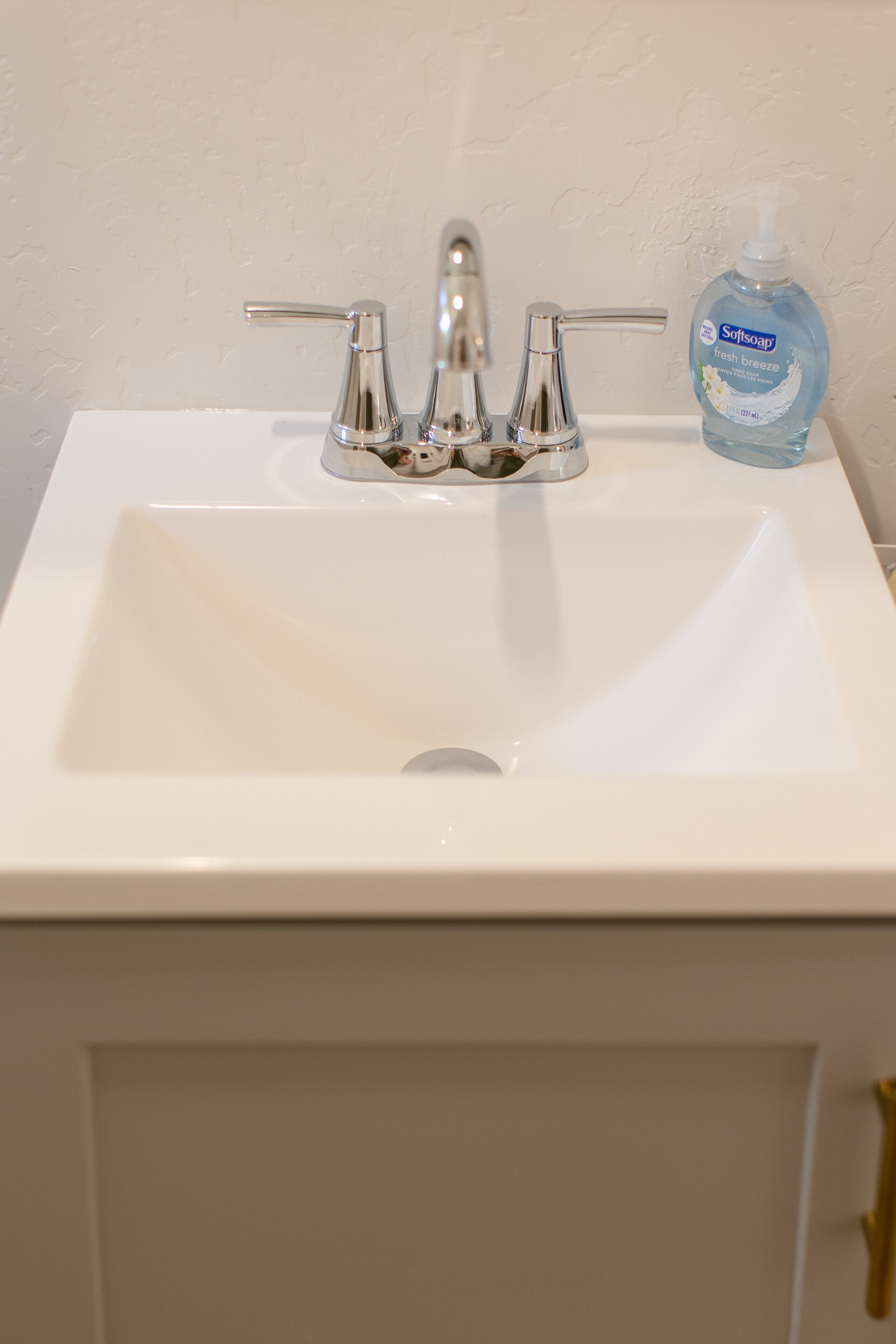 A white bathroom sink with a chrome faucet and a bottle of Softsoap Fresh Breeze.