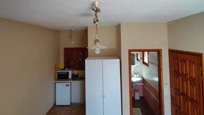 A compact kitchen with a refrigerator, microwave, and wooden cabinets. A door leads to a bathroom with a sink and mirror. - Georgias House Project First Floor (Skiathos)