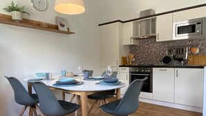 A modern kitchen with white cabinets, a microwave, and a stove. There is a dining table with blue chairs and a hanging light fixture.