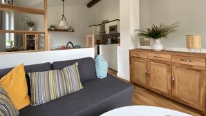 A modern living room with a dark grey sofa, wooden cabinets, and a kitchen in the background.