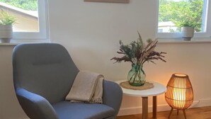 A modern room with a grey rocking chair, a small round table with a vase, and a floor lamp.