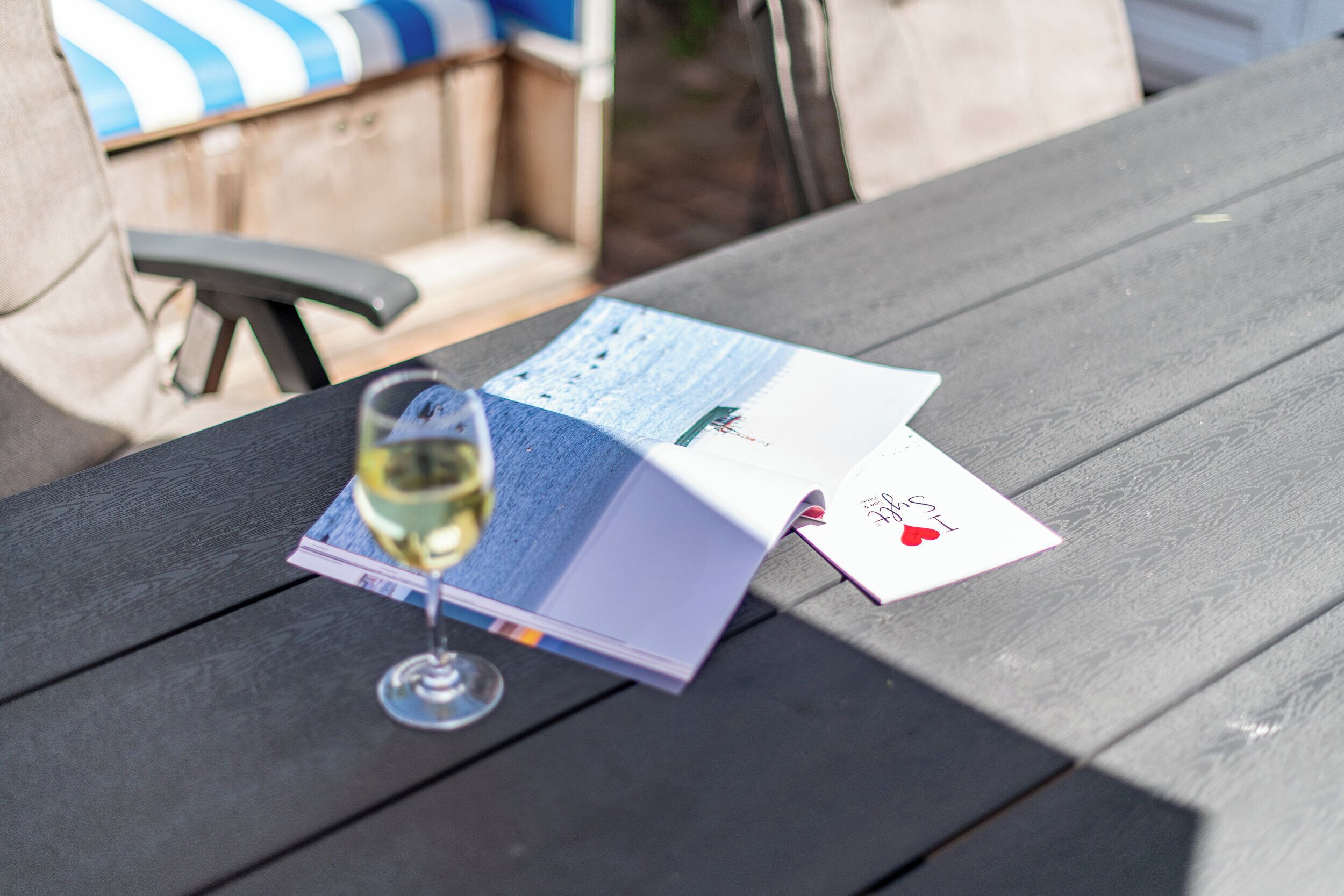 A wooden table with a glass of white wine, a brochure, and playing cards.