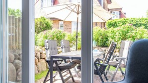 A patio with a table and chairs, a stone wall, and a house in the background. - Großzügig. Garten. Zentral. ID: Mbs/22 (Westerland)