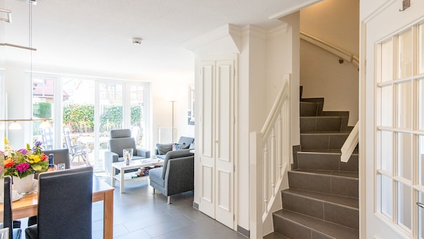 A spacious living area with a dining table, sofas, and a staircase leading to an upper floor. - Großzügig. Garten. Zentral. ID: Mbs/22 (Westerland)