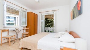 Un dormitorio con una cama, un escritorio y una silla. Hay una ventana y una puerta que da a un balcón.