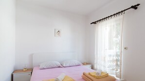 A bedroom with a bed, two pillows, a bedside table with a lamp, and a window with curtains.