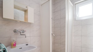 A bathroom with a white sink, a mirror, a shower enclosure, and a toilet.