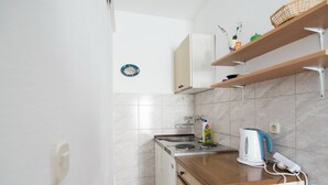 A compact kitchen with a sink, stove, and countertop. There are cabinets and a shelf above the counter.