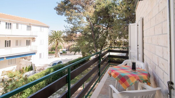 A balcony with a table and chairs, overlooking a street with parked cars and buildings.