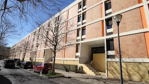 A multi-story building with a brick facade, a central staircase, and a parking lot with cars. - Charming 1-Bedroom Apartment, Balcony, WiFi, Near Thermal Baths, 2-Star Rating (Balaruc-les-Bains)