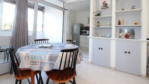 A dining area with a table set for four, a kitchen with a microwave and refrigerator, and a white cabinet with shelves. - Charming 1-Bedroom Apartment, Balcony, WiFi, Near Thermal Baths, 2-Star Rating (Balaruc-les-Bains)