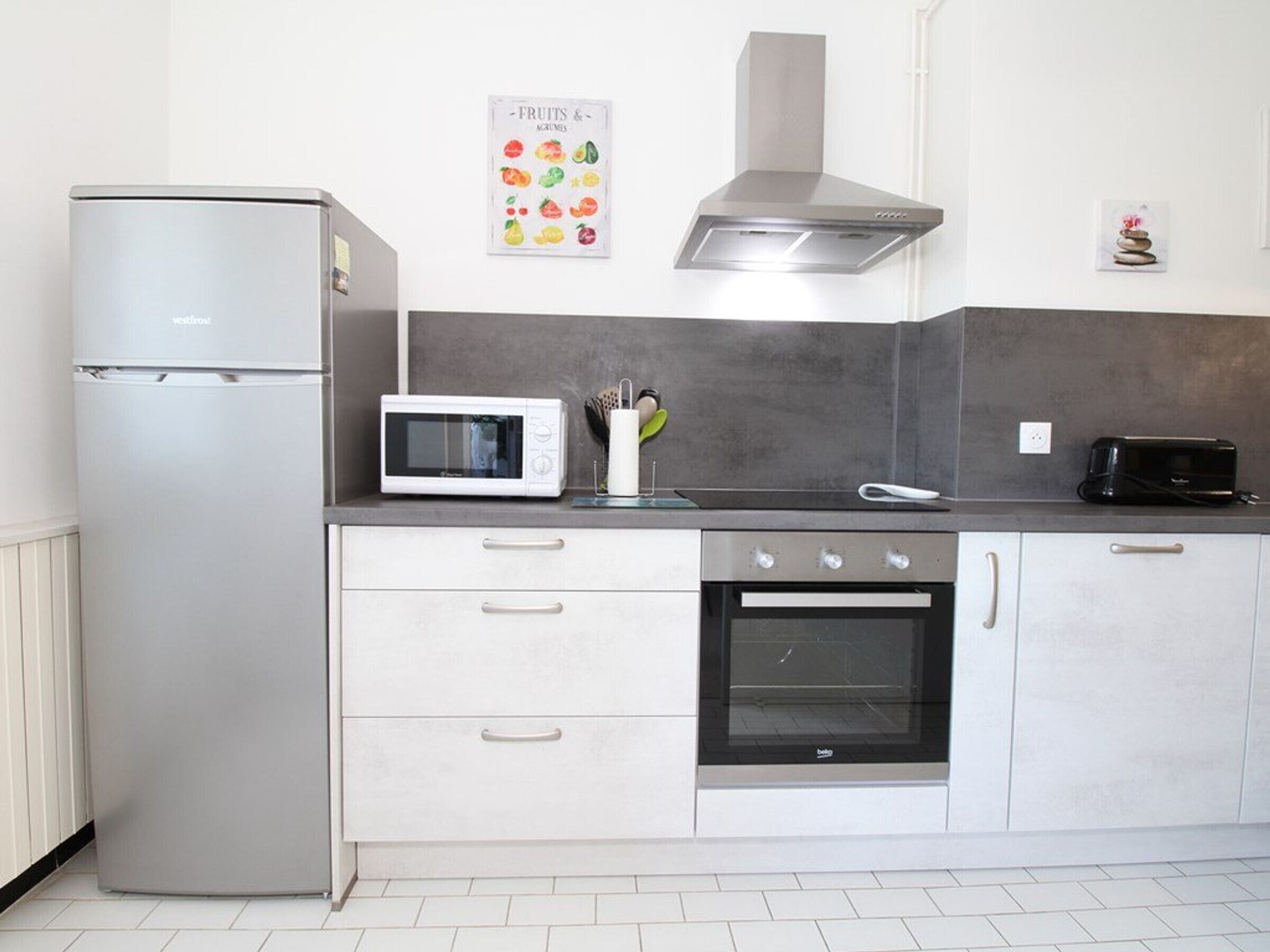 Eine moderne Küche mit Kühlschrank, Mikrowelle, Toaster, Backofen und einer grauen Arbeitsplatte.