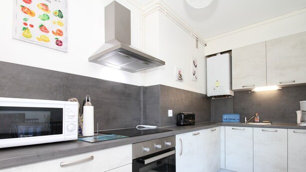 A modern kitchen with white cabinets, a built-in oven, a microwave, and a toaster. - Charming 1-Bedroom Apartment, Balcony, WiFi, Near Thermal Baths, 2-Star Rating (Balaruc-les-Bains)