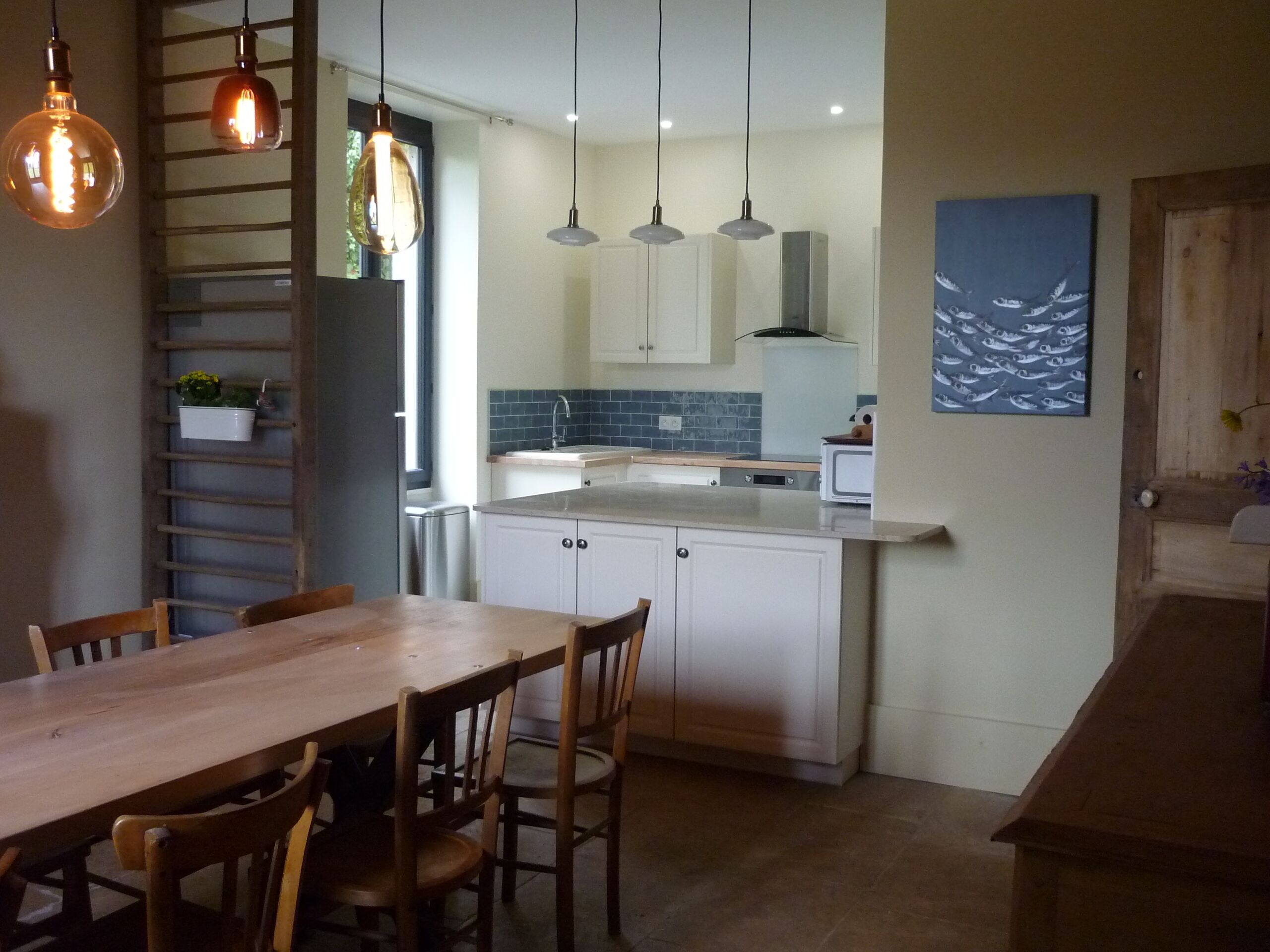 Une cuisine moderne avec des meubles blancs, une table à manger en bois et des luminaires suspendus.