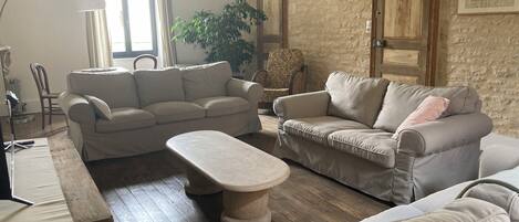 Ein Wohnzimmer mit zwei Sofas, einem Couchtisch und einer Lampe. Im Raum steht eine Pflanze und ein Sessel.