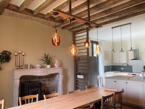 A dining area with a wooden table and chairs, a fireplace, and hanging pendant lights. - The Presbytery, Spacious Family Home for 10 People, 4 Bedrooms (Touillon)