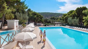 A swimming pool with sun loungers and umbrellas, surrounded by trees and a view of a hilly landscape. - Gattarella Family Resort - Self-catering accommodations in the pinewood  (Vieste)