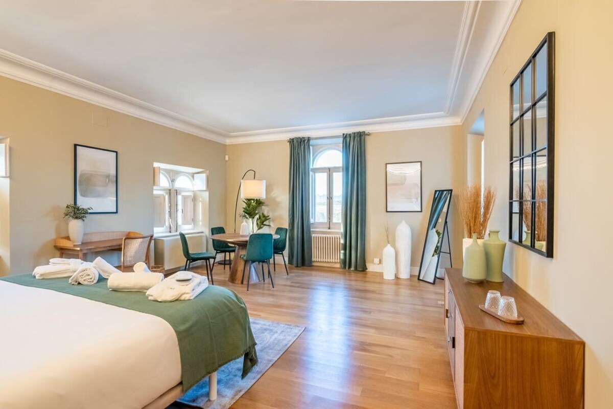Une chambre d’hôtel comprenant un lit, un bureau, une chaise, une fenêtre avec des rideaux et un miroir fixé au mur.