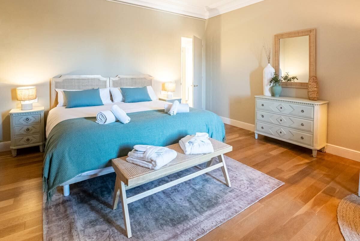 Une chambre bien rangée, avec un lit, des tables de chevet, une commode et un banc sur lequel sont posées des serviettes.