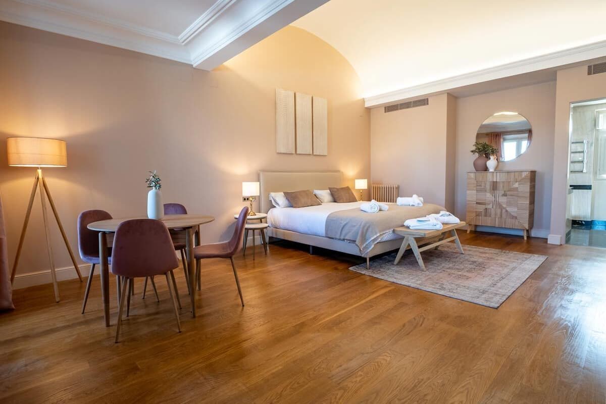 Ein modernes Hotelzimmer mit einem großen Bett, einem Essbereich mit Tisch und Stühlen sowie einer kleinen Sitzecke mit einer Lampe.