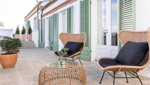 Une terrasse dotée de meubles en osier, d’une table en verre et de plantes en pot.