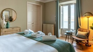 Une chambre d’hôtel avec un lit, une chaise, une petite table, un miroir et une vue sur l’extérieur, visible à travers une porte.
