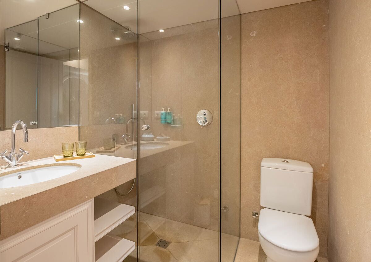Een moderne badkamer met een douchecabine van glas, een witte wastafel en een toilet.