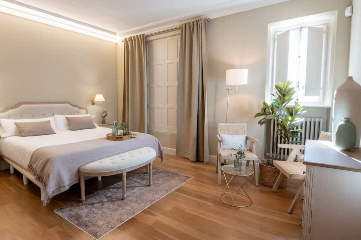Ein Schlafzimmer mit einem großen Bett, Nachttischen, einer Bank, einem kleinen Tisch und einem Sessel.