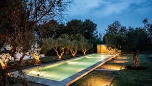 Une piscine rectangulaire dont le bord est recouvert de carrelage, entourée d’une pelouse bien entretenue et d’arbres.