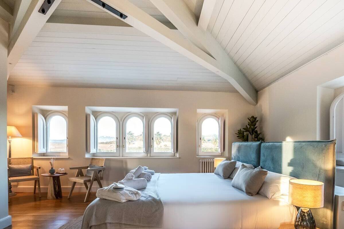 Ein Schlafzimmer mit einem großen Bett, einer Sitzecke mit Tisch und mehreren Fenstern mit Blick.