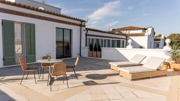 Una terraza en la azotea con comedor, sillones de descanso y plantas en macetas.