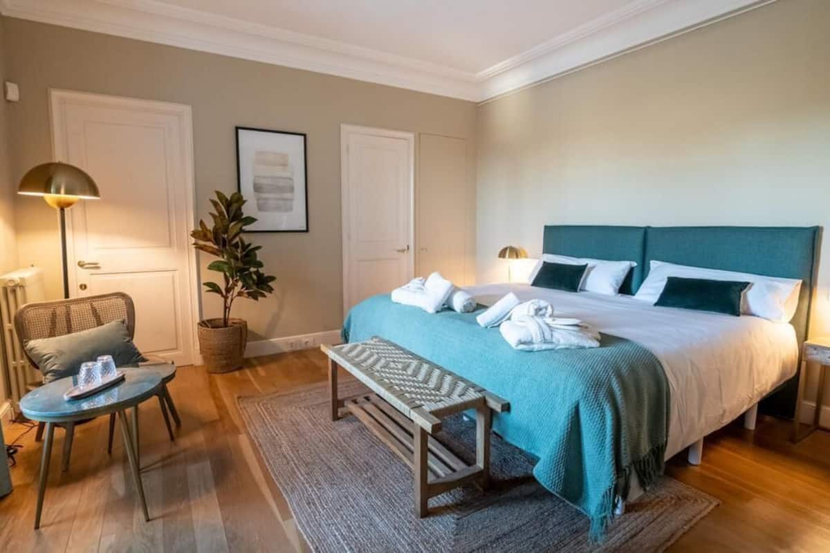 Ein ordentlich eingerichtetes Schlafzimmer mit Bett, Nachttischen, einem Sessel, einem kleinen Tisch und einer Topfpflanze.