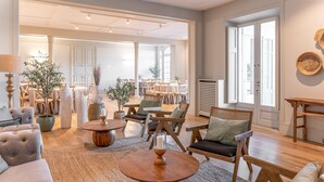 Un vaste espace de vie comprenant un canapé, une table basse ronde et plusieurs fauteuils. On y trouve également des plantes en pot et une cheminée.