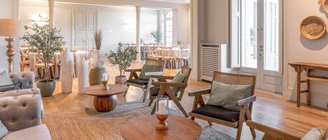 A spacious living area with a sofa, round coffee table, and multiple chairs. There are potted plants and a fireplace.