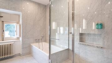Un baño moderno con cabina de ducha de vidrio, una bañera y un estante empotrado con artículos de aseo.