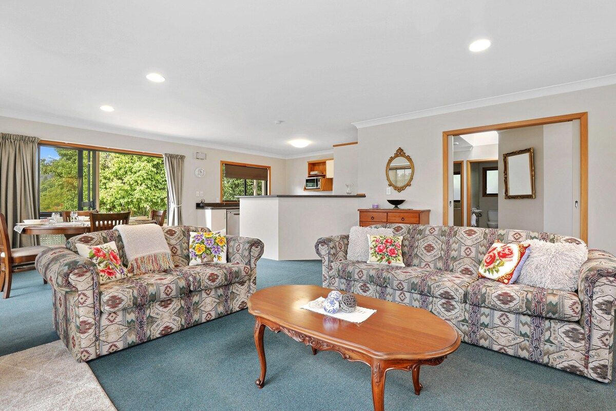 A spacious living area with two patterned sofas, a wooden coffee table, and a kitchen in the background.