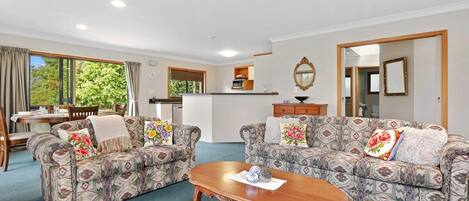 A spacious living area with two patterned sofas, a wooden coffee table, and a kitchen in the background.