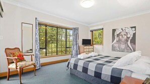 Une chambre d’hôtel avec un grand lit, une chaise en bois, un bureau avec un téléphone et une fenêtre avec des rideaux.