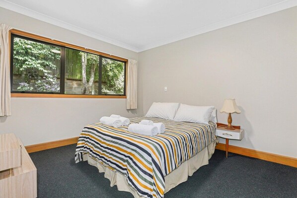 A hotel room with a bed, a nightstand, a lamp, and a window with curtains.