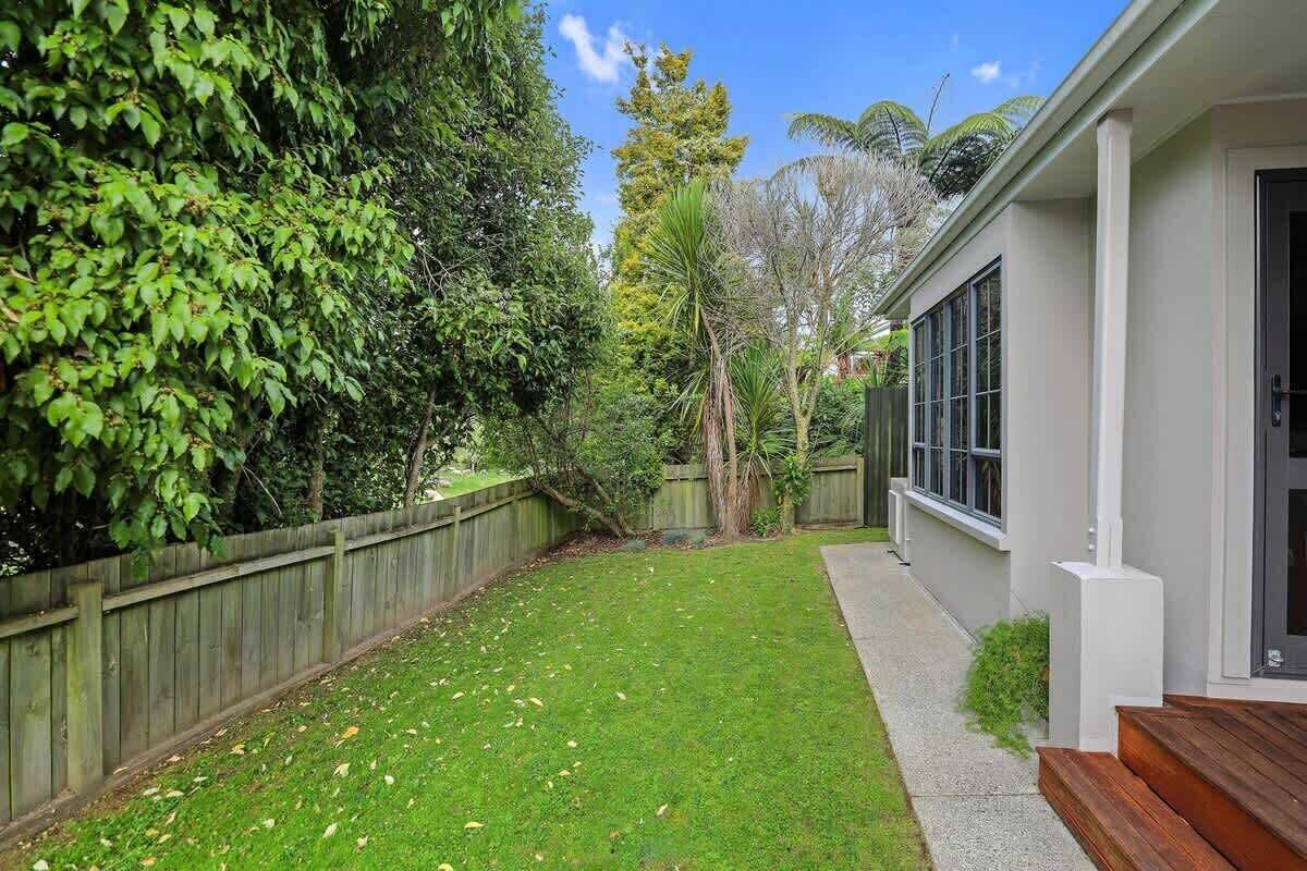 A residential backyard with a wooden fence, a lawn, and a house with large windows.
