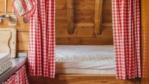 A cabin interior with a wooden floor, a bed with white bedding, and red and white checkered curtains. - Holiday Home in Ruinerwold With Garden (Ruinerwold)