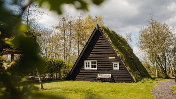 A triangular house with a sloped roof, a bench in front, and a small window. - Holiday Home in Ruinerwold With Garden (Ruinerwold)