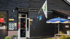 A wooden building with a door open, a flag, and a blue umbrella. - Holiday Home in Ruinerwold With Garden (Ruinerwold)