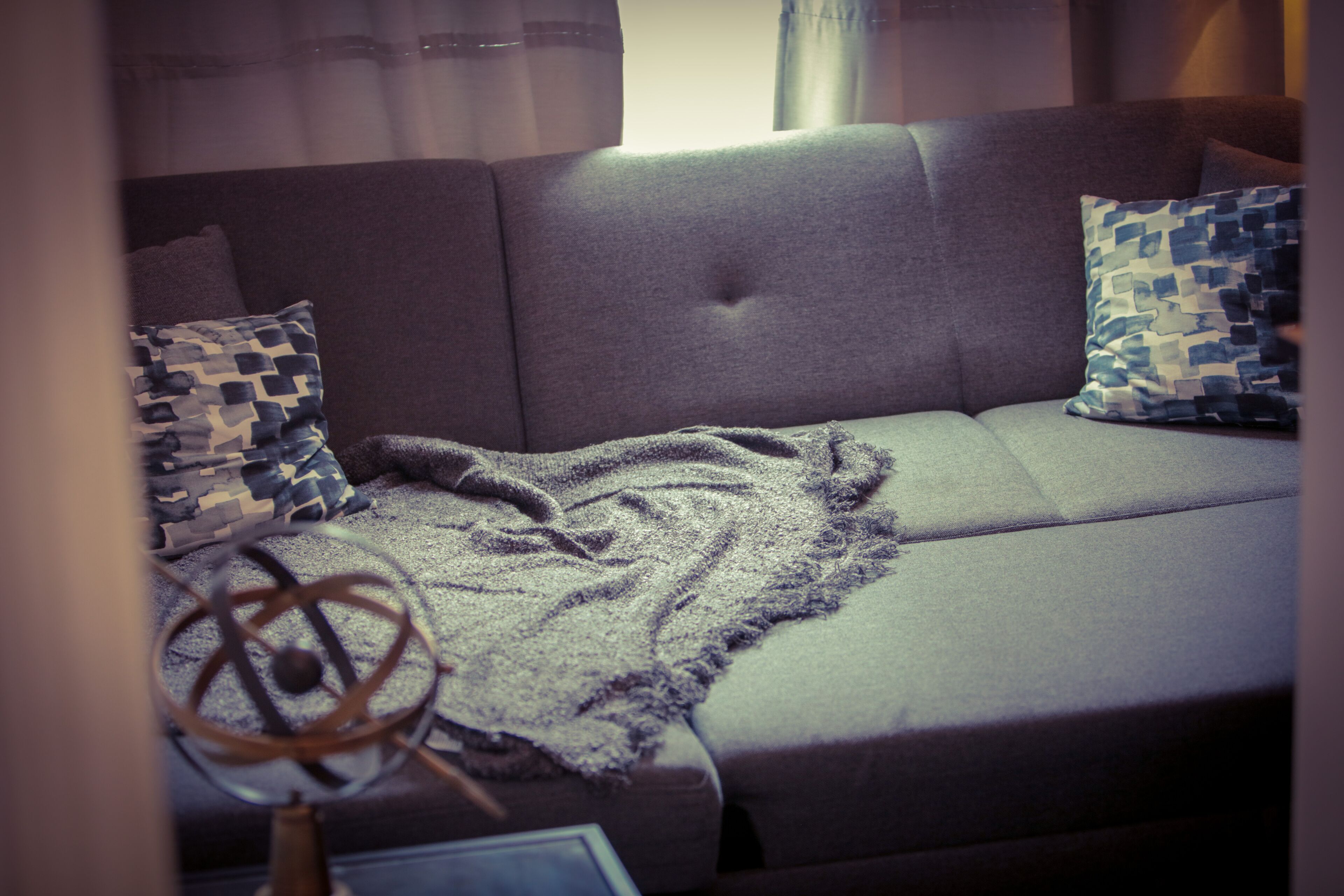Un canapé gris agrémenté de coussins à motifs, d’un plaid et d’un objet décoratif posé sur une table.