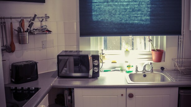 A compact kitchen with a microwave, toaster, sink, and a window with blinds. - Warren st Apt (London)